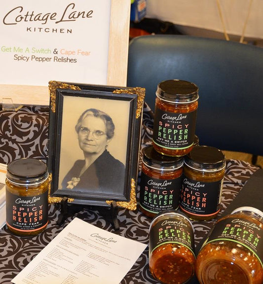 photo of spicy pepper relish bottles with a framed black and white photo of a woman and a sign saying Cottage Lane Kitchen