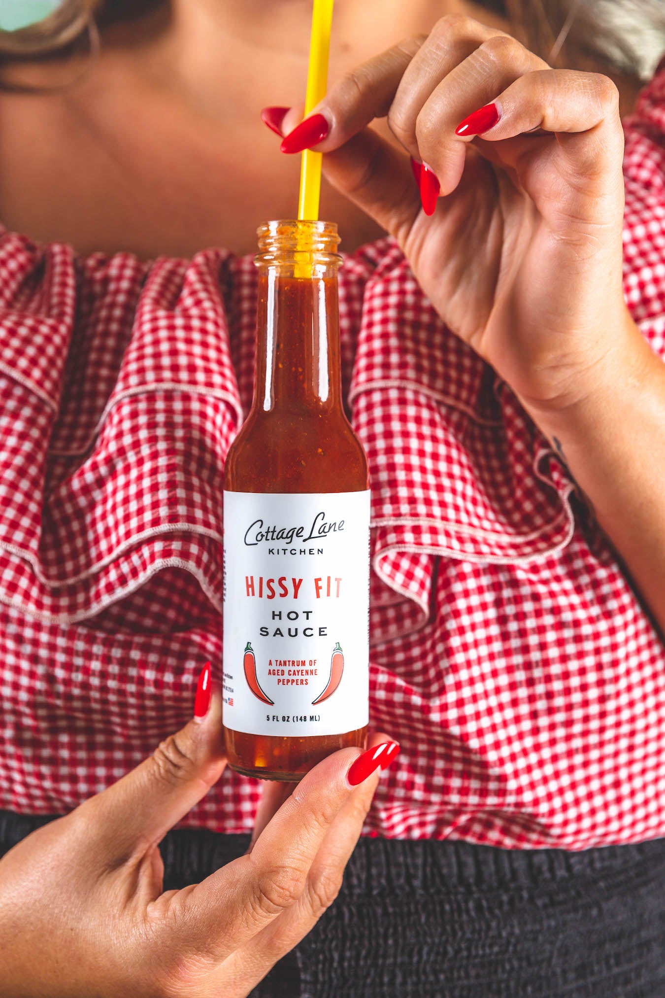 Hissy Fit Hot Sauce bottle open and woman drinking it with a yello straw straight from bottle