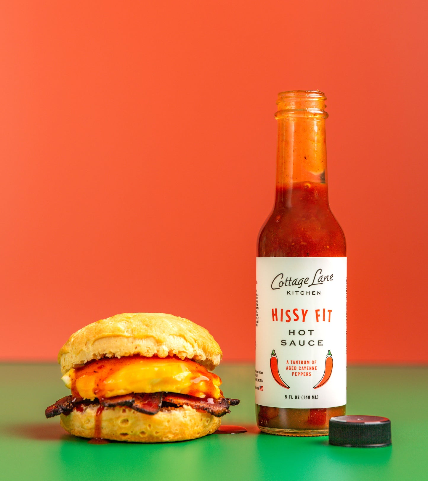Photo of Hissy Fit Hot Sauce on Egg and Bacon Biscuit with bright red background