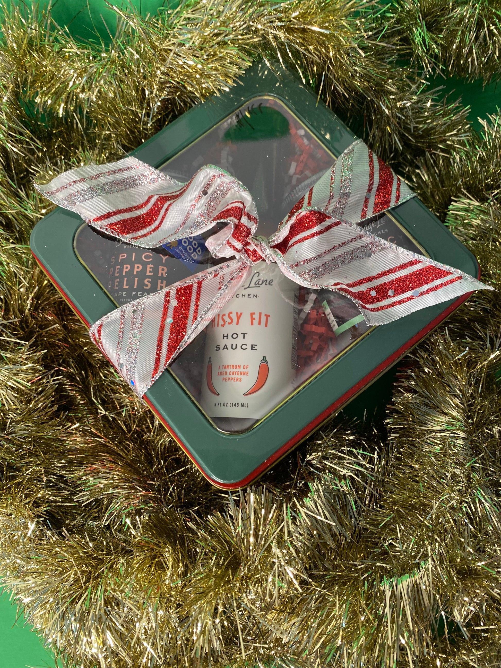 Holiday gift set of Cottage Lane Kitchen products wrapped in a box with a red and white ribbon surrounded by tinsel